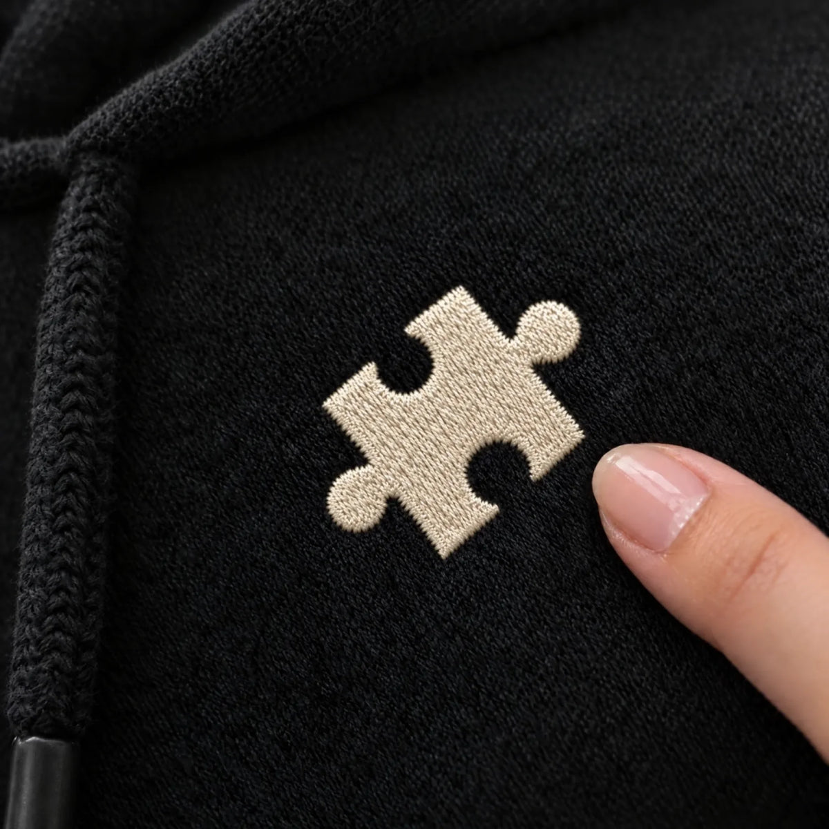 Detail: gesticktes Puzzleteil auf schwarzem Hoodie